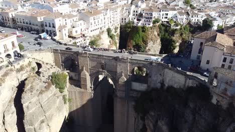high drone view of puente nuevo bridge connecting cliffside streets in ronda with deep rocky gorge below and rows of white buildings forming a striking contrast against natural terrain.