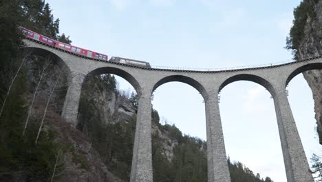 Traditional-red-Swiss-panorama-train-passing-on-a-stone-bridge-viaduct-in-Landwasser-Brucke