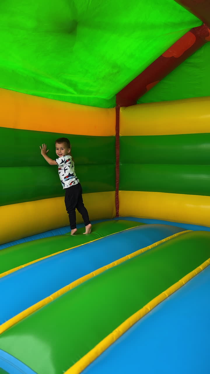 Energetic baby boy runs, falls and tumbles cheerfully inside the inflatable playhouse. Happy active fun time spending. Vertical video.