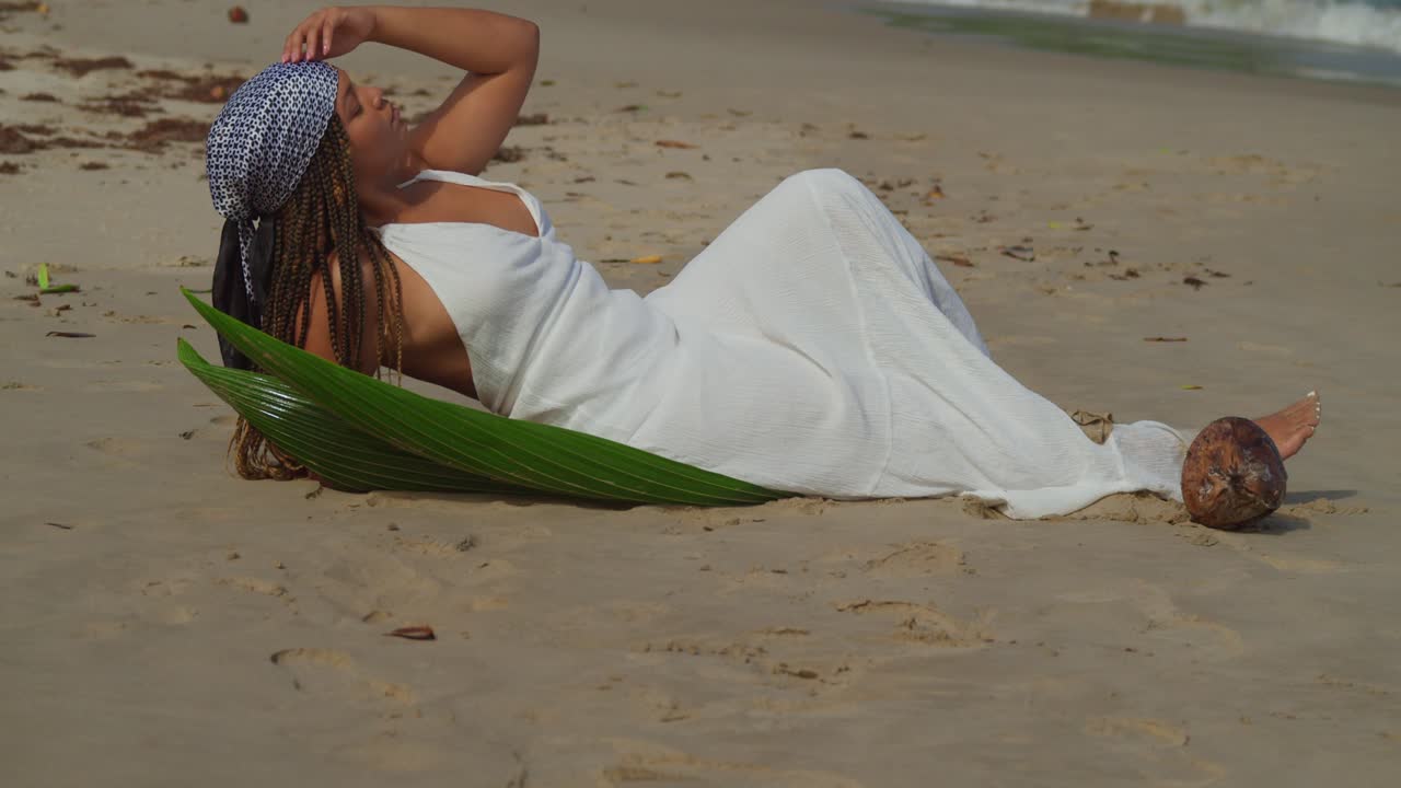 Cô gái trẻ nằm trên cát vàng óng của một hòn đảo Caribe với những con sóng vỗ vào bờ ở phía sau.