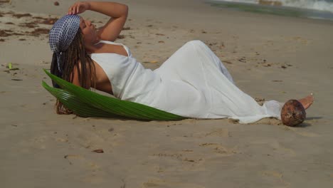 young female lays in the golden brown sand of a caribbean island with waves crashing in the background