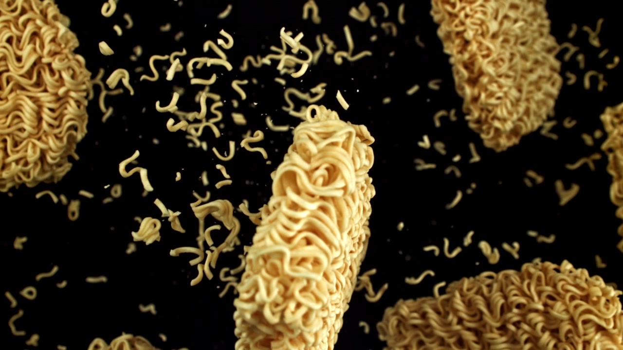 Noodles istantanei secchi che cadono al rallentatore su sfondo nero