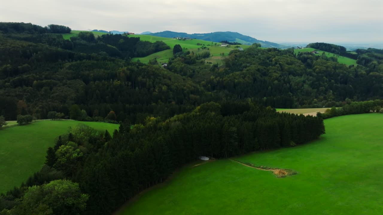 Smooth aerial flight over green meadows, grain fields and forested hills in Kürnberg, Austria. Dolly in aerial