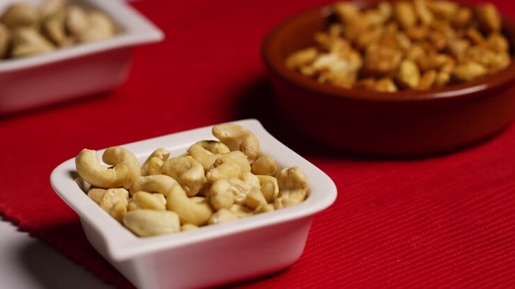 Close Up Of Hand Choosing From Bowl Of Cashew Nuts In Studio