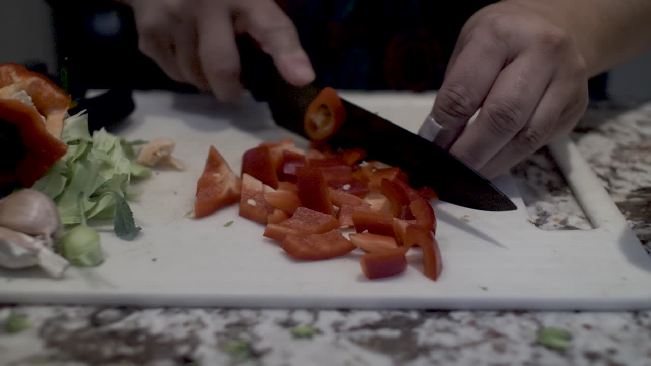 vista de cerca del cocinero cortando pimientos rojos en el tablero de la cocina
