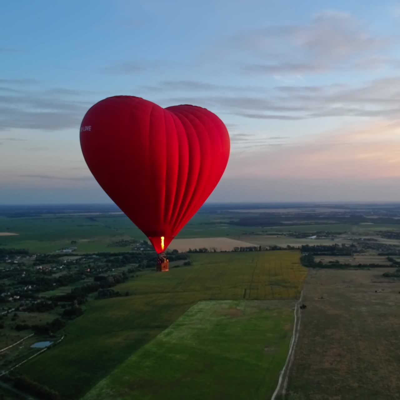 Red airship in the shape of a heart. Hot air balloon in the sky over a field in the countryside flying in the beautiful evening sky.