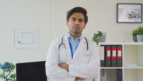 Portrait-Of-Serious-Male-Doctor-Or-GP-With-Stethoscope-Wearing-White-Coat-Standing-In-Office