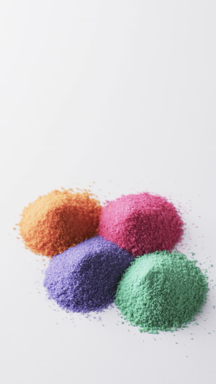Vertical video of close up of multi coloured sand grains and copy space on white background