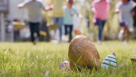 Gruppe-Von-Kindern-Mit-Hasenohren,-Die-Auf-Der-Ostereiersuche-Im-Garten-Laufen,-Um-Schokoladeneier-Zu-Holen