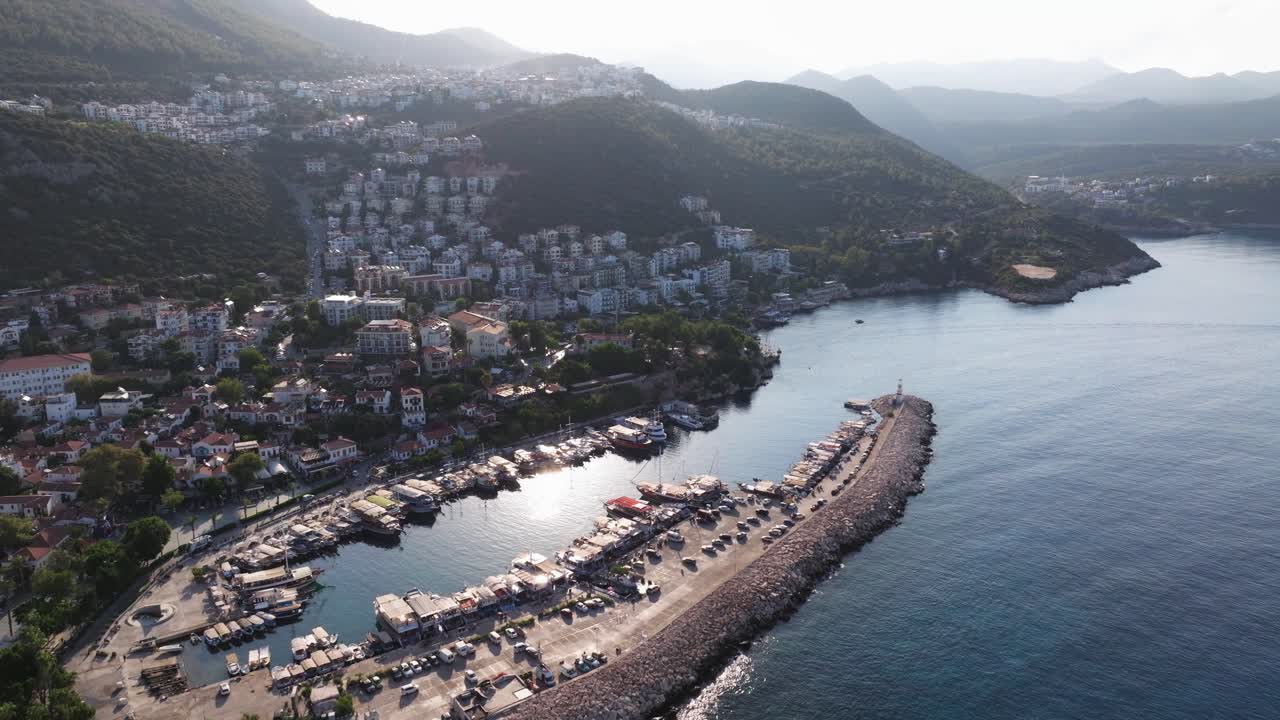 Aerial dolly of Kas marina in Antalya, Turkey, with boats docked in the harbor and beautiful clear waters glistening from sun in the Mediterranean