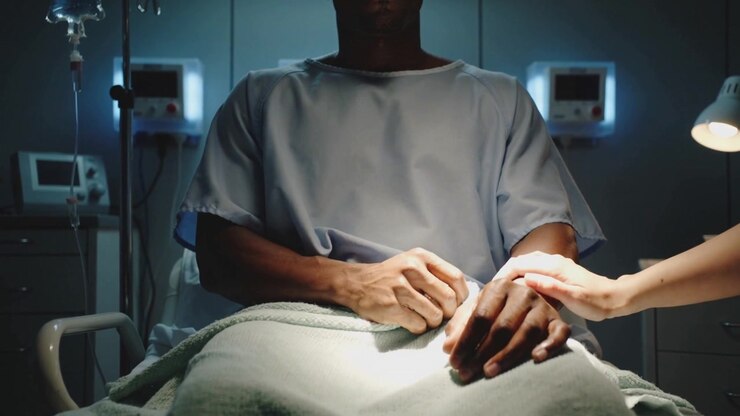 Mano di un accompagnatore che si protende, tiene la mano destra del paziente nel letto d'ospedale in camice, per conforto, dispositivo.