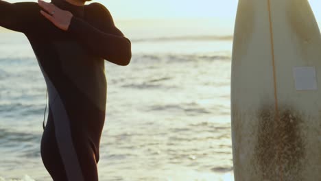 Side-view-of-mid-adult-caucasian-male-surfer-stretching-and-warming-up-before-surfing-at-beach-4k