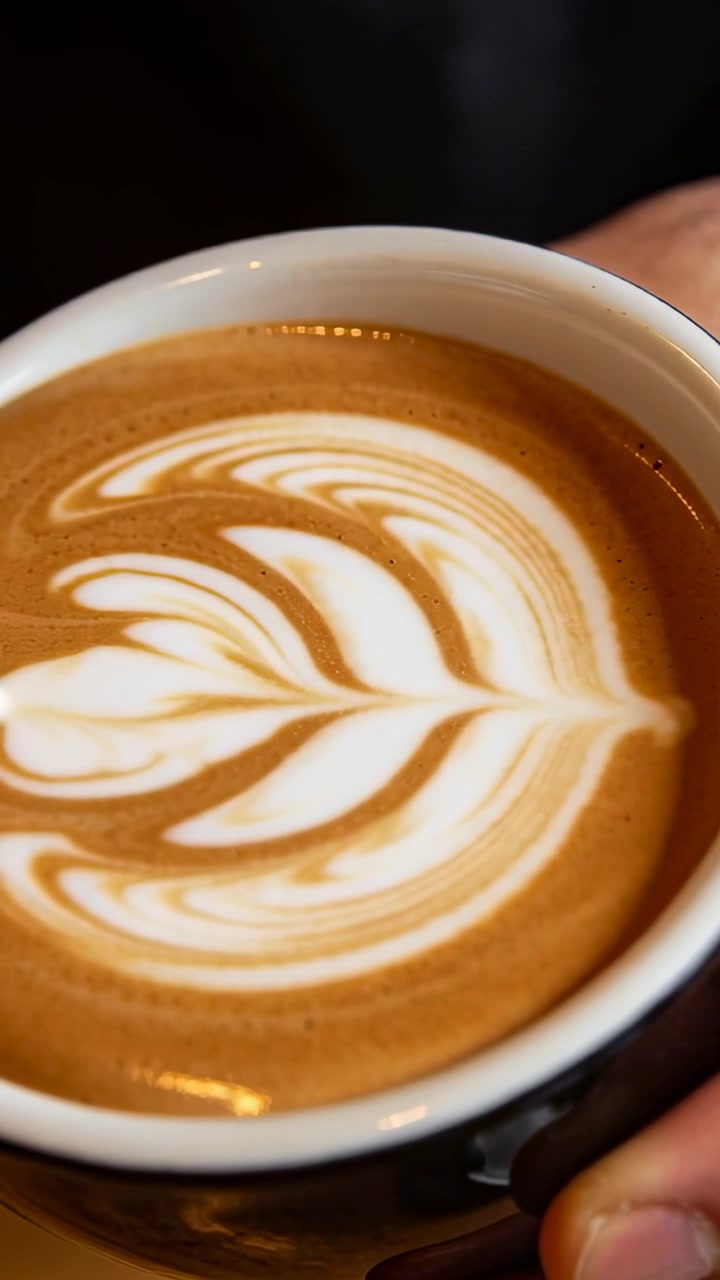 Video vertical: Barista vertiendo y formando una roseta en la taza en una cafetería, terminando el diseño con una jarra