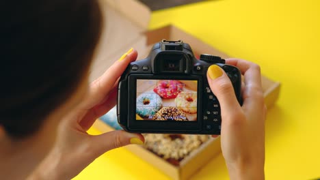 woman's hands take pictures with photo camera of delicious donuts in box