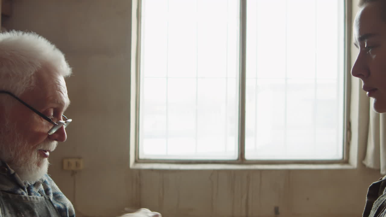 노인 도자기 가 작업실 에서 젊은 여자 견습생 과 대화 하고 있다