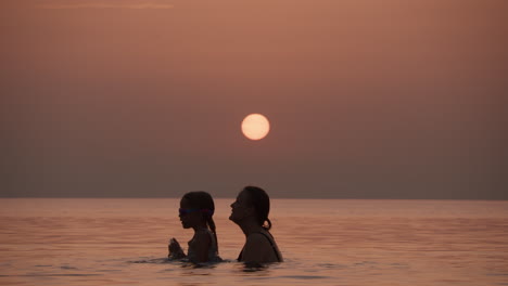 mother and daughter playing in the ocean at sunset