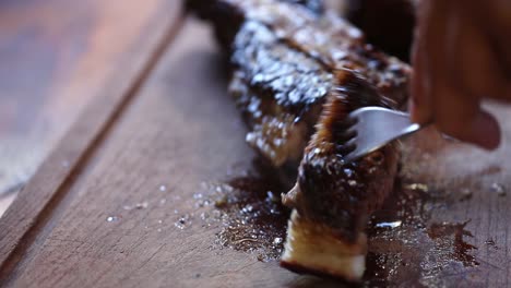 close up view of male hand with a knife slicing a piece of meat on cutting board