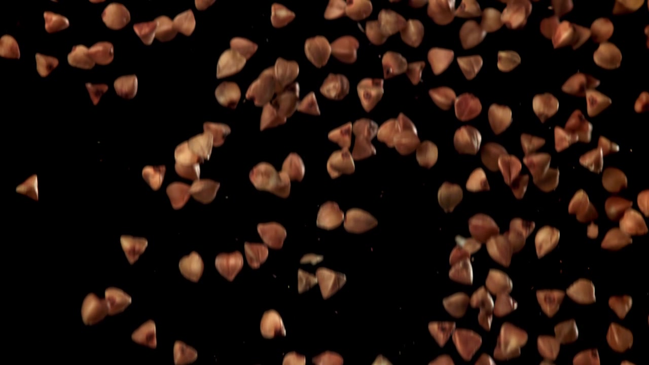 Grani di grano saraceno in caduta al rallentatore su sfondo nero