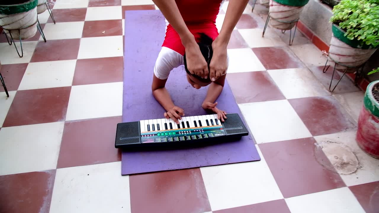 la cámara se acerca a una joven india haciendo yoga tocando un teclado con ambas manos y poniendo sus pies en el aire mientras hace yoga