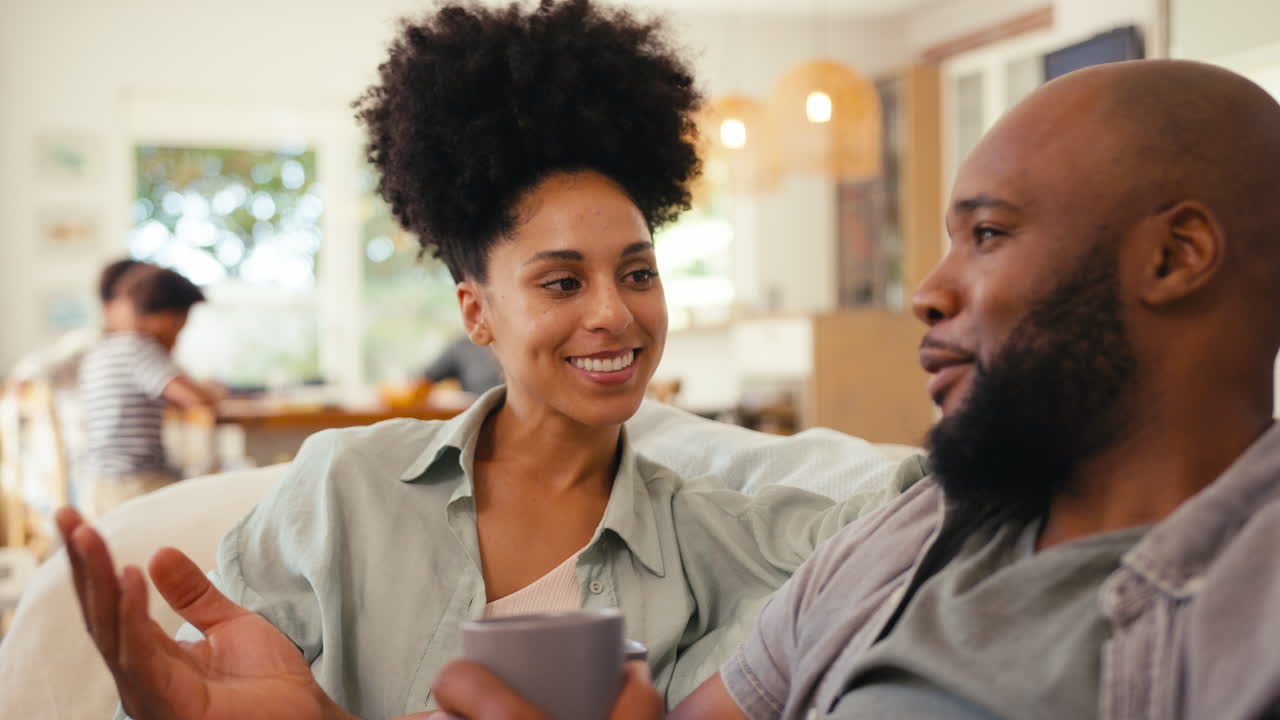 Couple At Home On Sofa Streaming Show Or Movie To TV With Multi-Generation Family In Background
