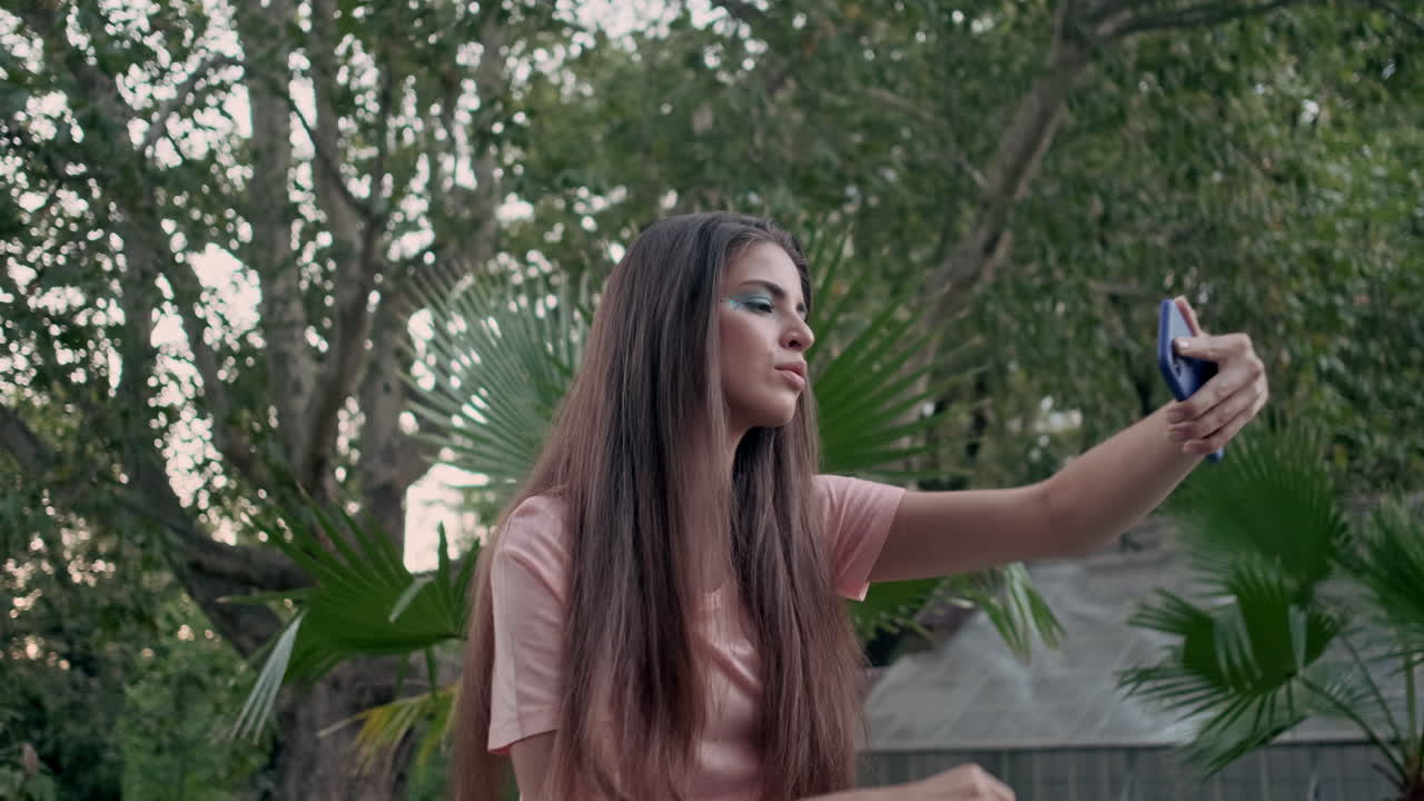 Joven modelo tomándose una selfi con plantas tropicales de fondo.