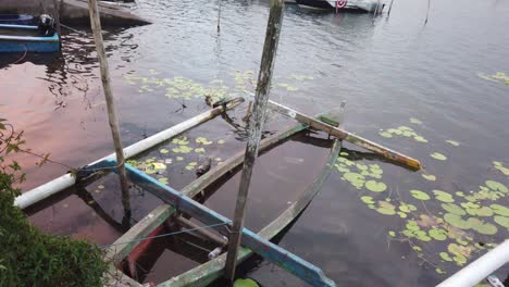 A-canoe-in-Beratan-Lake-in-Bali,-Indonesia-that-is-submerged-by-water-in-the-boat-slip,-surrounded-with-lily-pads