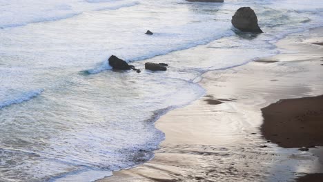 waves hitting rocks on a sandy beach