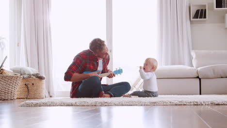 Vater-Spielt-Mit-Seinem-Kleinen-Sohn-Ukulele-Im-Wohnzimmer