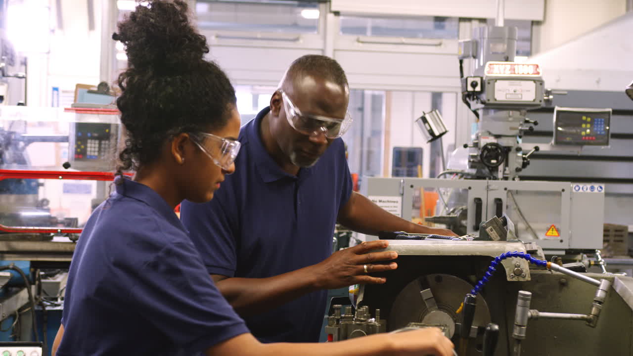 Engineer Showing Female Teenage Apprentice How To Use Lathe