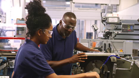 engineer showing female teenage apprentice how to use lathe