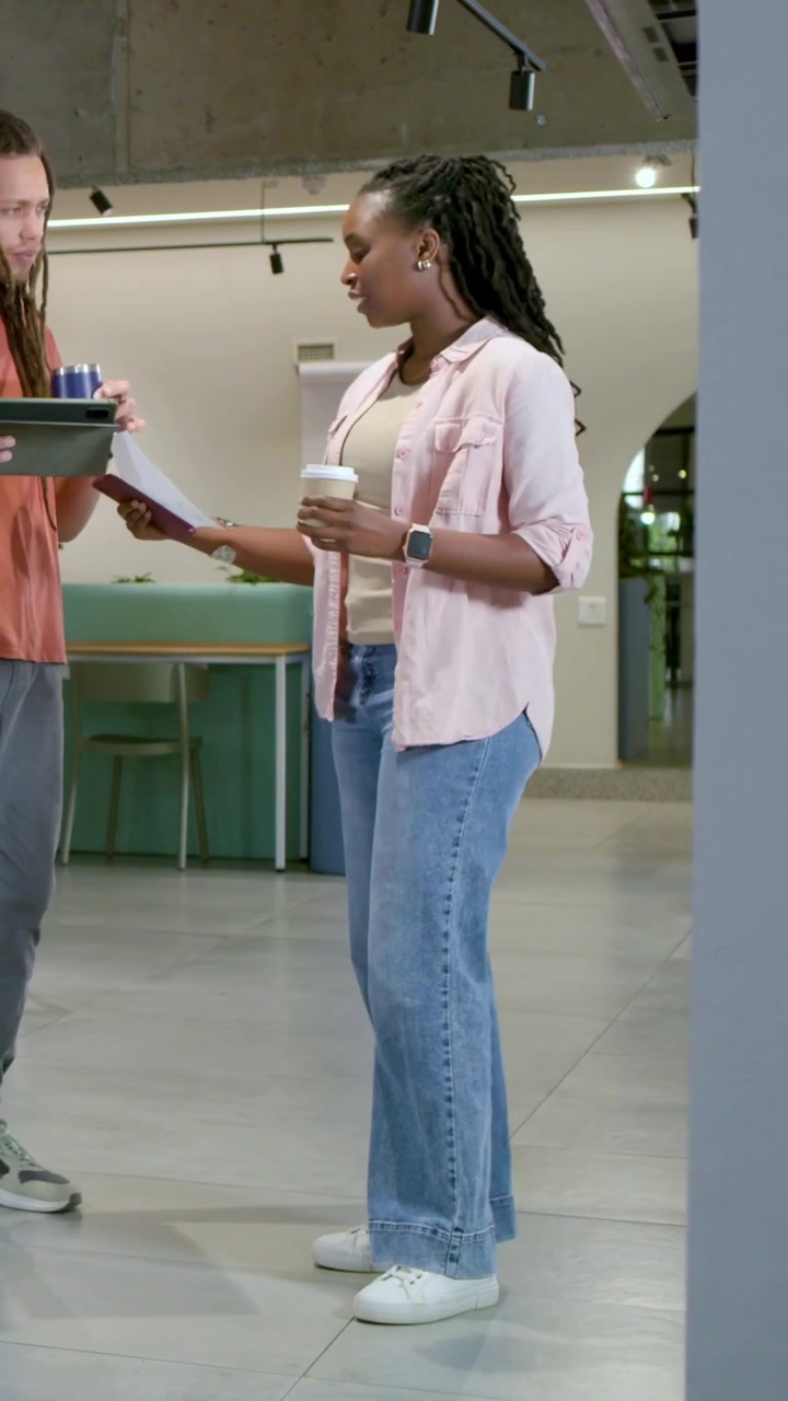 Vertical video: Walking duo leaving lounge in coral, pink checking tablet, paper confirming details