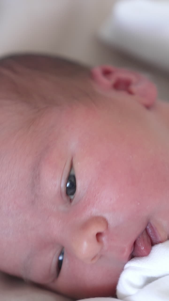 Face of adorable newborn baby. Portrait of healthy cute infant child boy on the bed at home. Happy family relationship and newborn baby. Close-up Vertical video