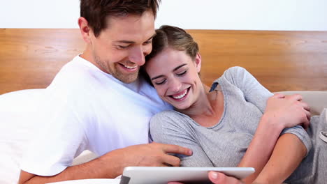 pareja feliz acostada en la cama usando la tableta juntos