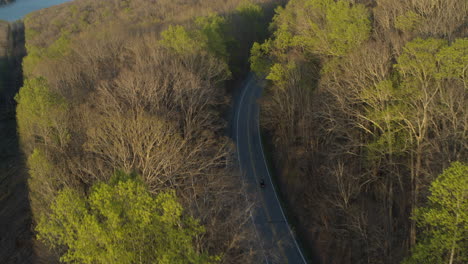 aerial footage following a motorcycle that is driving on curving roads amongst spring trees