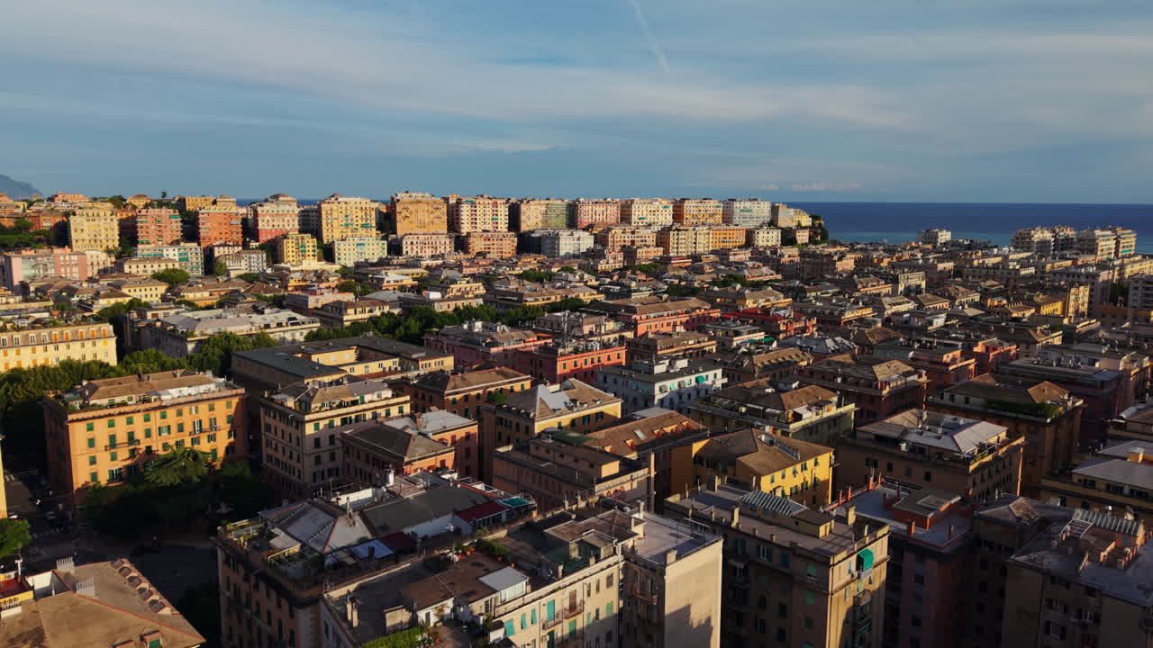 Aerial drone forward shot above Genoa, showing Vittoria Square, rooftops, hillside blocks, and the sea in the distance at sunset