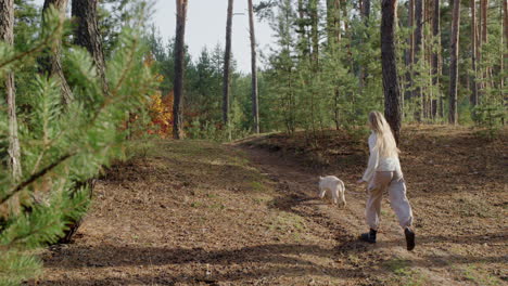 a teenage girl runs with a dog along a path in a pine forest.