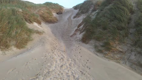 a drone ascends over hvide sande beach as strong winds sweep sand across the dunes on a stormy day, capturing the dramatic movement of nature against denmark’s rugged coastline