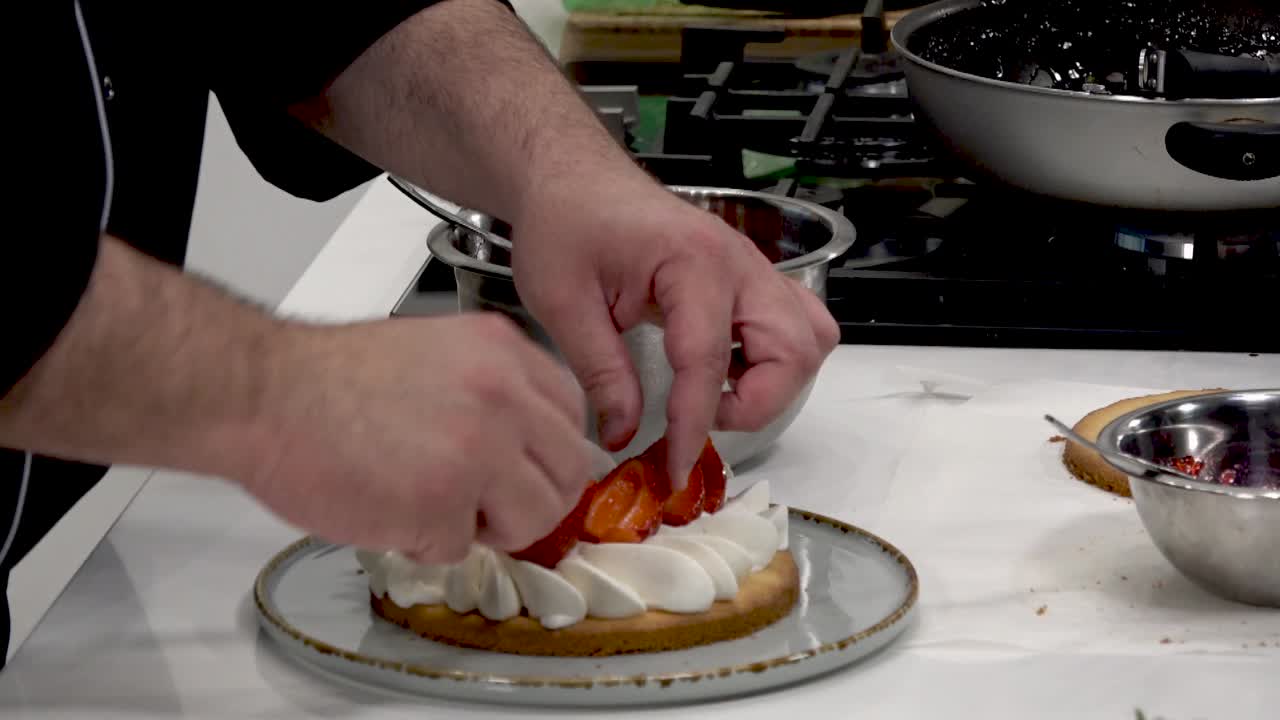 A talented chef carefully assembles a dessert by adding freshly cut strawberries and cream on a cake base during a culinary demonstration in a contemporary kitchen