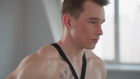 close up of boy bare torso adjusting resistance rope during workout session in naturally lit room, showcasing toned body, with soft background of window and indoor light