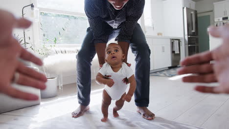 point of view shot of parents encouraging smiling baby son to take first steps and walk at home