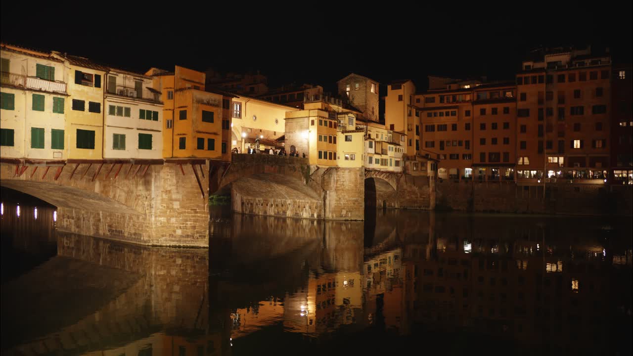 Ponte Vecchio a Firenze illuminato di notte con il riflesso sul fiume.
