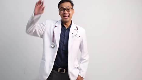 Friendly young male doctor of Asian ethnicity look around for friend find waving meet greet with hand as notices someone isolated on white background studio portrait