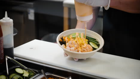 worker drizzles spicy mayo sauce over traditional hawaiian poke salad bowl, slow motion 4k