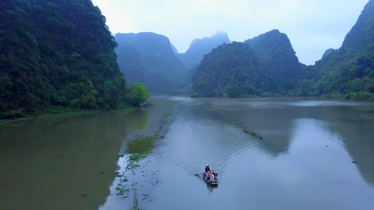 Cinematic drone footage of majestic limestone peaks in misty and foggy weather. Ricefields in wild jungle in the spring with boat tour canal in Tam Coc, Ninh Binh, Vietnam