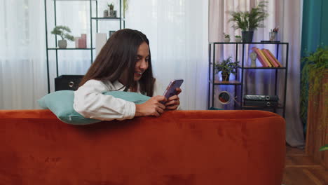 Portrait-of-adult-girl-sitting-on-sofa,-using-smartphone-share-messages-on-social-media-application