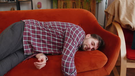 exhausted young alcoholic drunk man flopped down on couch falls asleep after party tired overworked