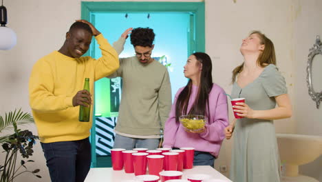 happy multiethnic young friends playing beer pong at home