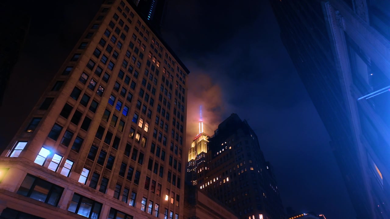 Empire State Building tra grattacieli scuri. Vista dell'Empire State Building incorniciato da edifici per uffici in una notte nuvolosa a New York