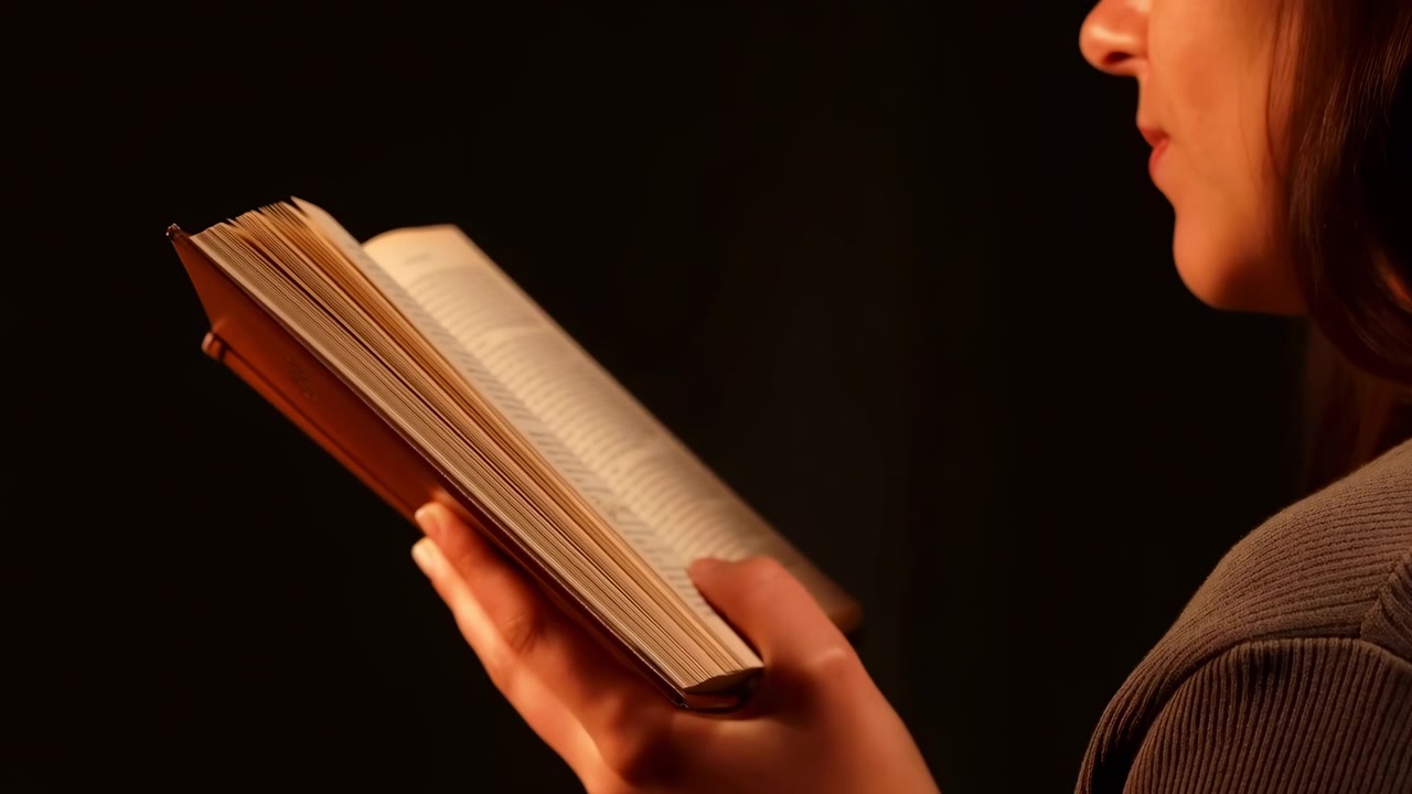 Una donna è profondamente assorta nella lettura di un libro in un ambiente sereno e poco illuminato, circondata dal bagliore soffuso di luci calde, creando un'atmosfera calma e concentrata.