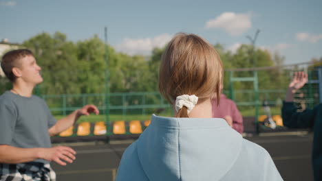 close up back view of lady wearing cyan hoodie playing volleyball with teammates, background features other people engaging in game, showcasing outdoor volleyball session under clear sky